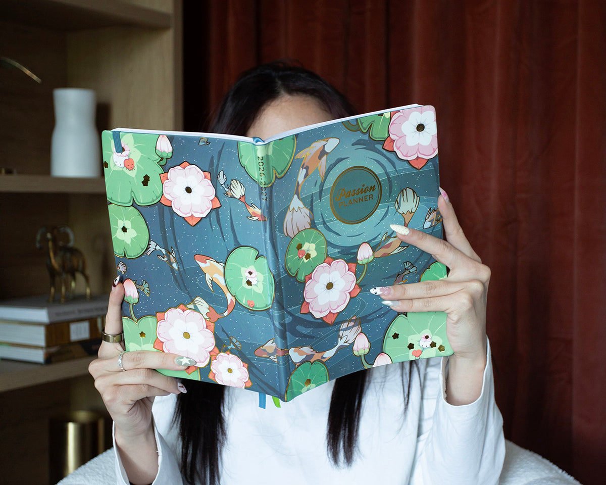 Person holding a weekly planner with a colorful floral and koi fish design.