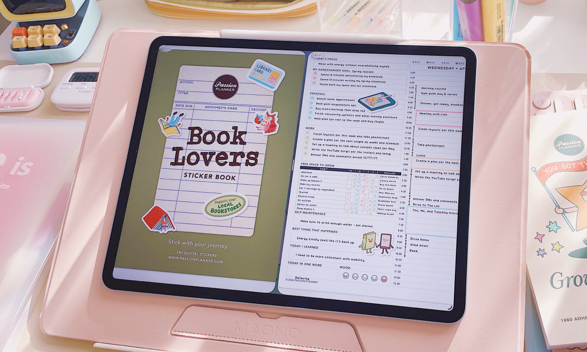 Tablet displaying a 'Book Lovers' sticker book app on a pink surface with stationery items.