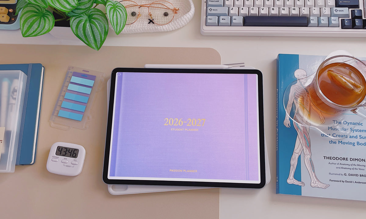 Tablet displaying a 2026-2027 digital calendar on a desk with books, a keyboard, and a plant.