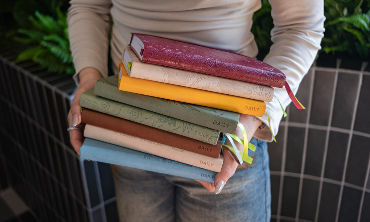 Person holding a stack of colorful journals against a blurred indoor background