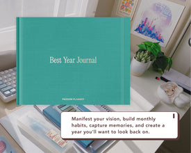 A teal Best Year Journal by Passion Planner is displayed on a desk with a white text overlay that reads 'Manifest your vision, build monthly habits, capture memories, and create a year you'll want to look back on.'.
