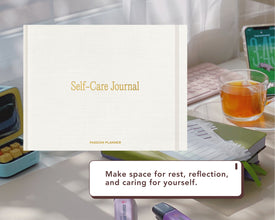 A white digital Self-Care Journal with gold lettering is shown in a styled desk setting with a glass of tea, a smartphone, and other office accessories. A text box at the bottom reads, 'Make space for rest, reflection, and caring for yourself.