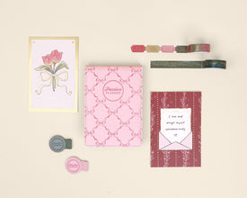 Collection of stationery items including a card with a tulip design, a pink notepad, and other stationery on a beige background.
