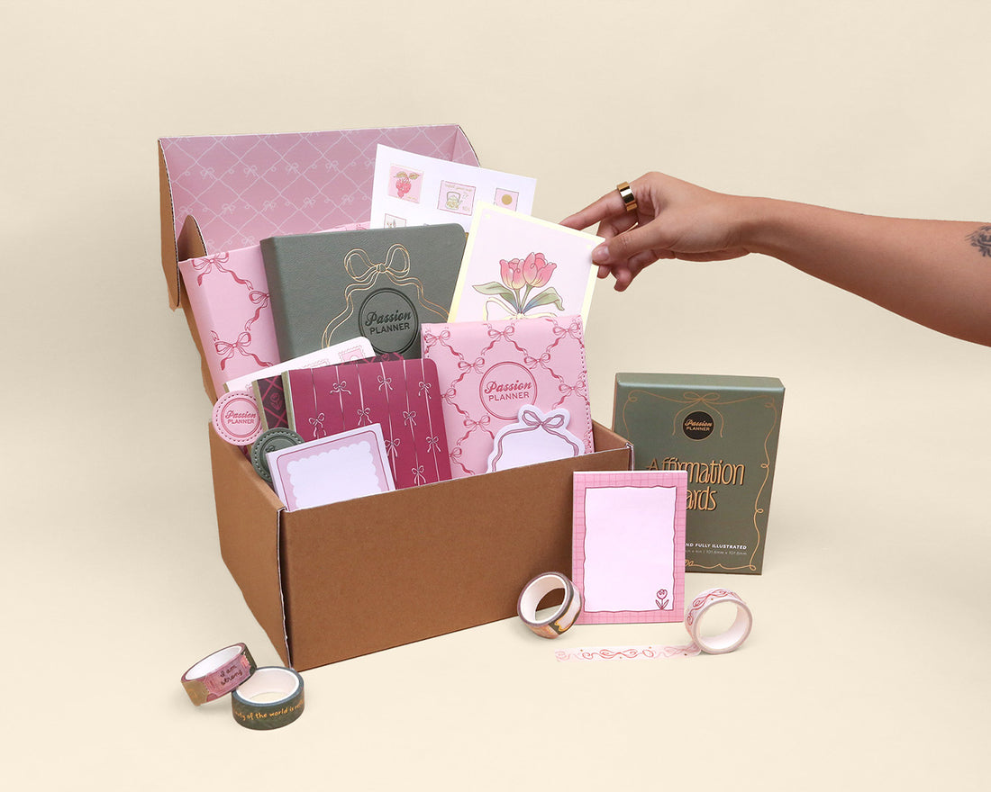 Collection of stationery items including notebooks and stickers in a box on a beige background