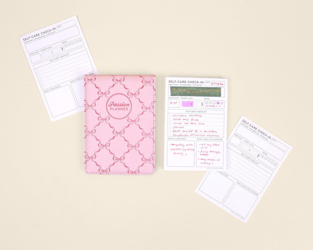 Pink notepad with self-care check-in sheets on a beige background