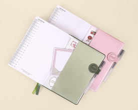 One pink and one green planner with a matching pen loop on a beige background
