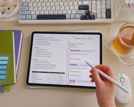 Person using a digital planner with a to-do list on a desk with a keyboard, notebook, and tea.